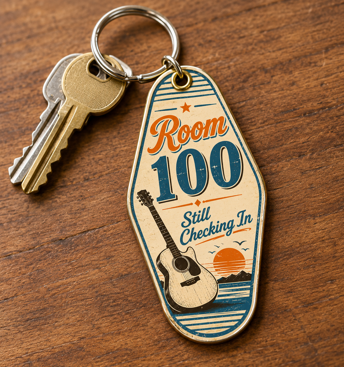 Vintage-style motel keychain reading "Room 100 Still Checking In" with guitar and sunset design, attached to keys on wood table