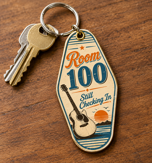 Vintage-style motel keychain reading "Room 100 Still Checking In" with guitar and sunset design, attached to keys on wood table